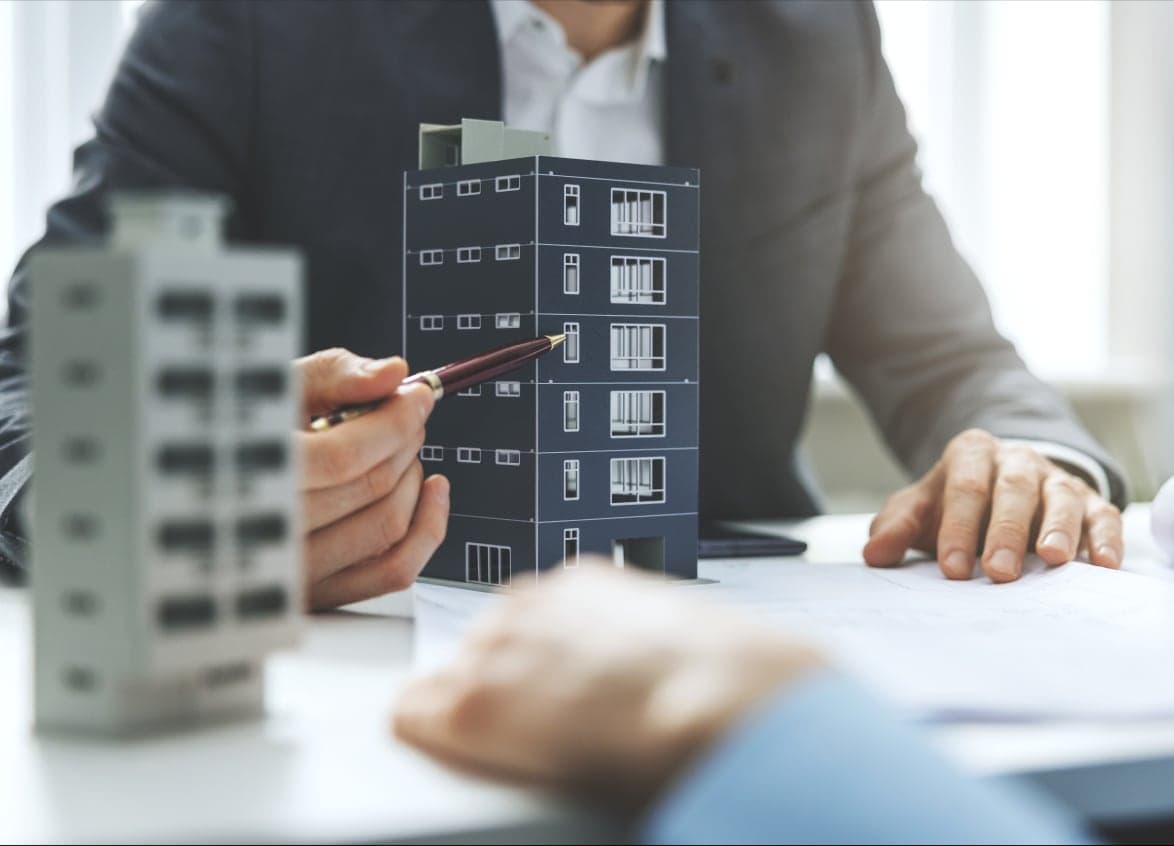 A Satnam Real Estate adviser pointing out a floor on a scale model of an apartment building, over site plans